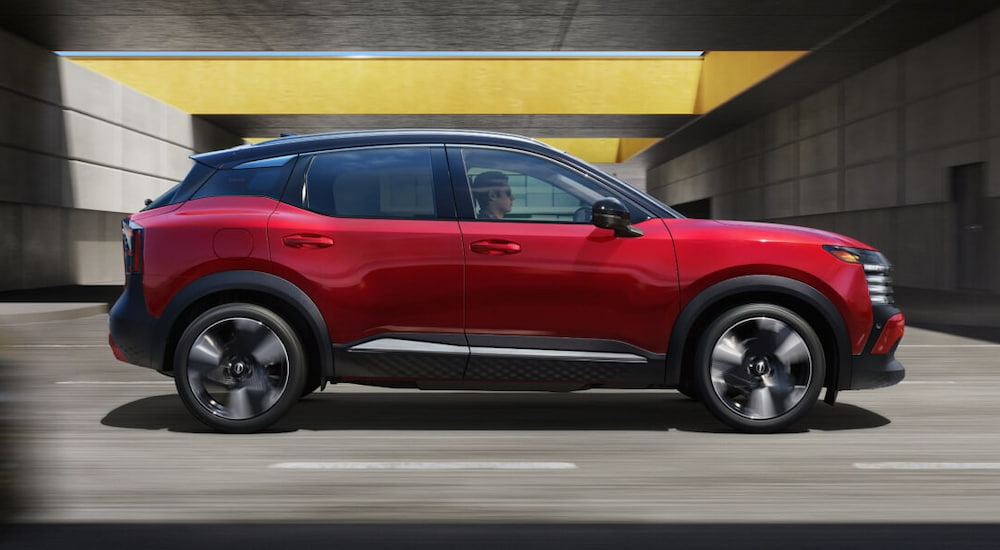 Side of a red 2025 Nissan Kicks SR driving down a road.