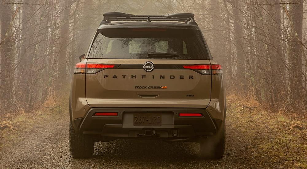Rear of a brown 2025 Nissan Pathfinder Rock Creek driving down a forest path.