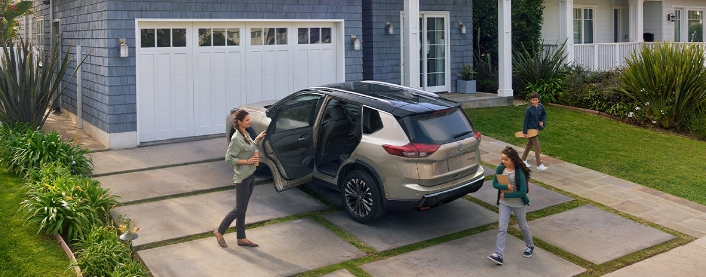 A tan 2025 Nissan Rogue is shown from the rear at an angle after leaving a Nissan dealer near Eagan.