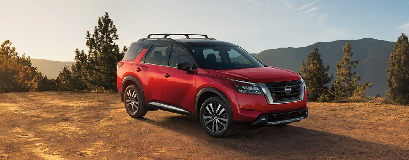 A red 2024 Nissan Pathfinder Platinum parked on a hilltop after visiting a Nissan dealer.