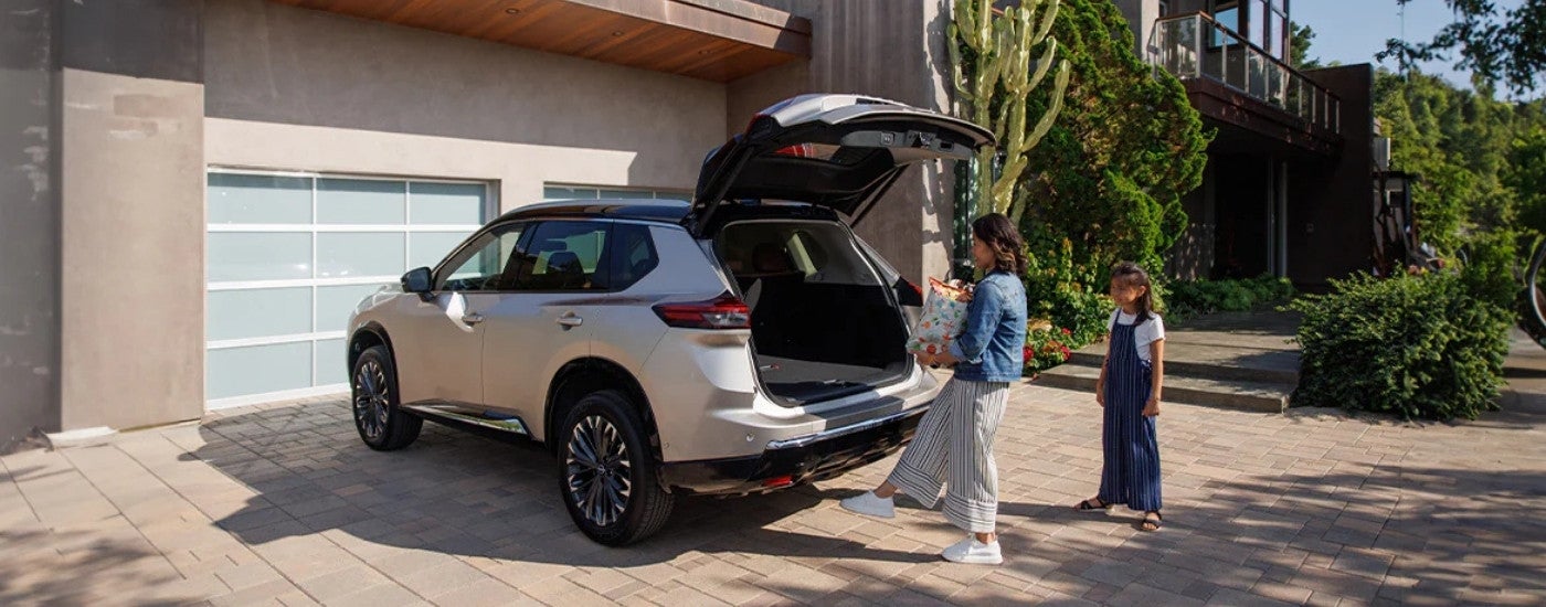 A woman using the motion activated liftgate on a 2025 Nissan Rogue Platinum parked in a driveway/