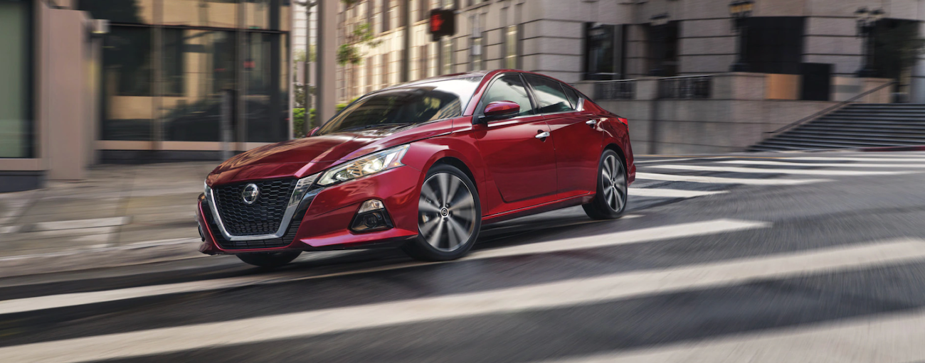 Red 2021 Nissan Altima driving through a city from a Nissan dealer near Shakopee.